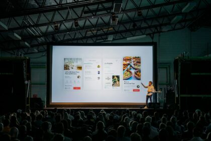 person discussing while standing in front of a large screen in front of people inside dim-lighted room